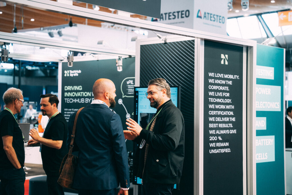 Ein Messestand von efs in Schwarz, Grün und Weiß. Davor unterhalten sich zwei Personen, einer davon von hinten zu sehen. Im Hintergrund stehen zwei weitere Personen, seitlich sichtbar, ebenfalls im Gespräch.